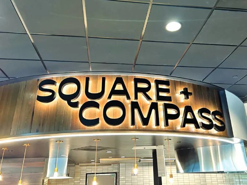 An image of the Square + Compass lit up interior signage.